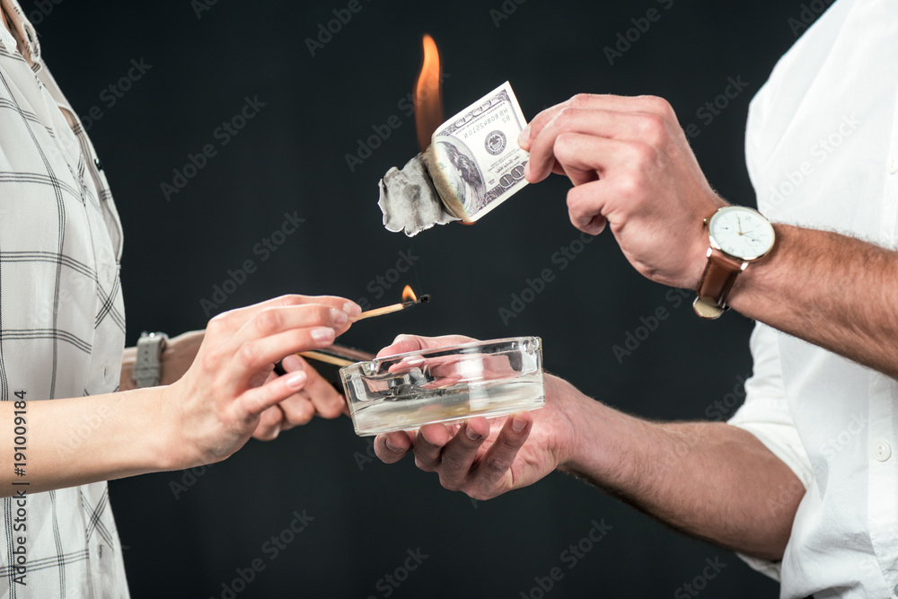 cropped view of businesspeople burning dollar banknotes, isolated on black