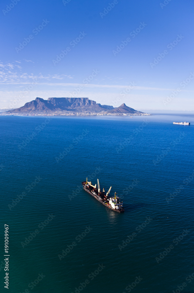 Aerial view of Cape Town, South Africa, with Table Mountain in the distance and a cargo ship in foreground.