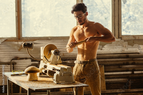 Turner working on a lathe in the workshop. Male hand carved wooden blank photo