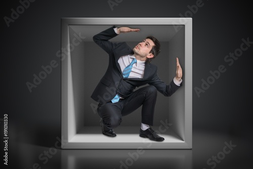 Young businessman trapped inside uncomfortable small box. photo