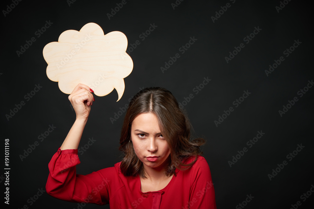 Discontent woman holding an empty thought bubble and looking at camera brooding, over dark background