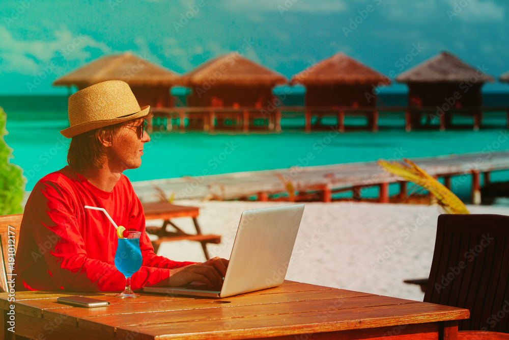 Young man with laptop and cocktail at luxury beach