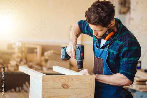 Carpenter drills a hole with an electrical drill photo