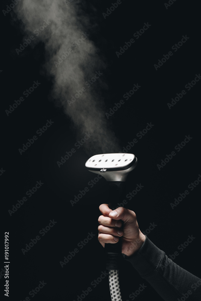Φωτογραφία close-up partial view of person holding garment steamer with steam on black