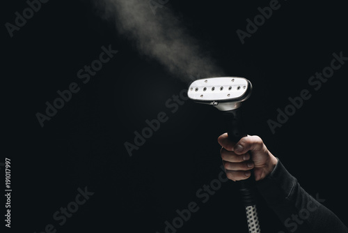 cropped shot of person holding garment steamer with steam on black photo