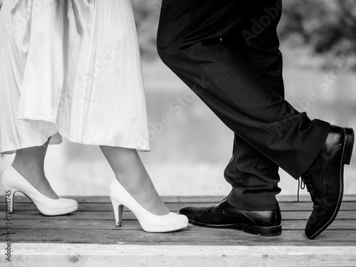 bride and bridal groom are standing on the bench and showing their shoes in black and white