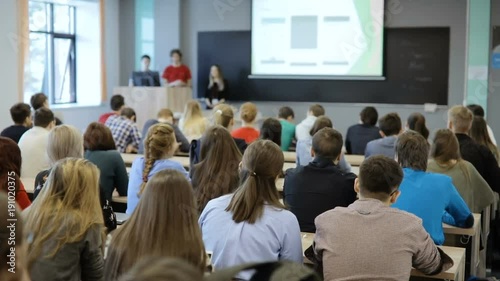 Group of university students sitting at their desks in auditorium and listening as their teacher holds a lecture.