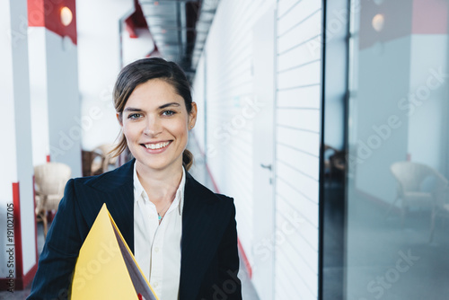 Portrait of smart casual dressed charming woman with paperwork standing in the office