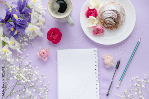 Coffee, clean notebook, eyeglasses and flower on purple table from above. Female working desk. Cozy breakfast. Flat lay style. top view. Delicious breakfast, sweet rolls