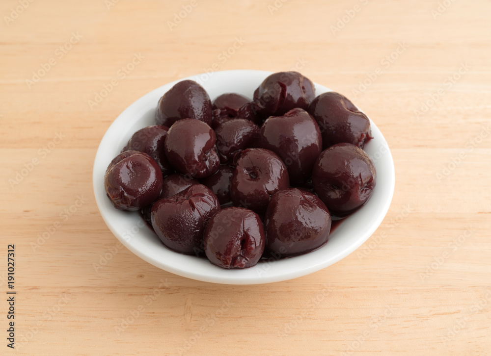 A small white bowl of sweet pitted cherries on a wood table. A small white bowl of sweet pitted cherries on a wood table.