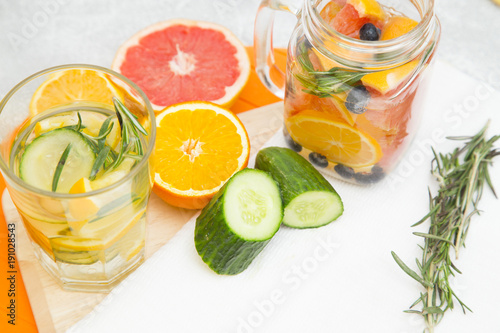 Detox infused water with slices of grapefruit, orange, lemon, cucumber, blueberry and rosemary on cutting board and white napkin