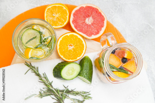 Detox infused water with slices of grapefruit, orange, lemon, cucumber, blueberry and rosemary on cutting board and white napkin, top view