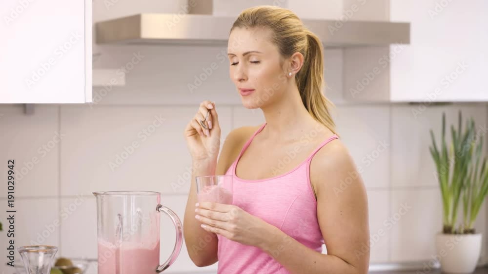 Sporty young woman tastes strawberry smoothie Sporty young woman tastes strawberry smoothie