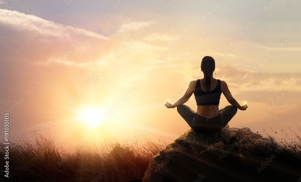 Woman practices meditating yoga at is an asana on a stone, sunset mountains background