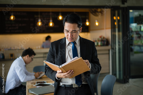 Canvas Print Asian businessman in black suit, who standing and holding document file about financial report on hand