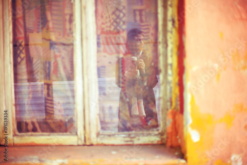 Woman photographer reflection in a window of an old house with bright facade and vintage curtains captured in Tirana, Albania