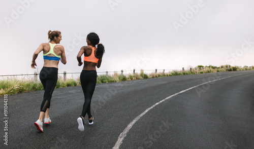 Two women athletes running on road