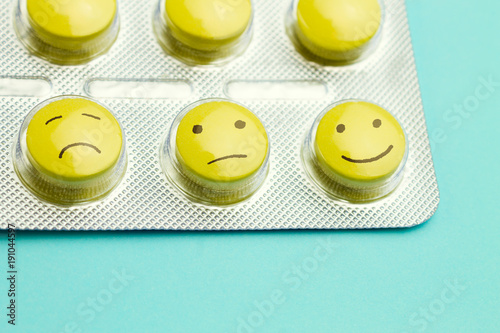 Yellow pills and  funny faces in a blister on a blue background. The concept of antidepressants and healing