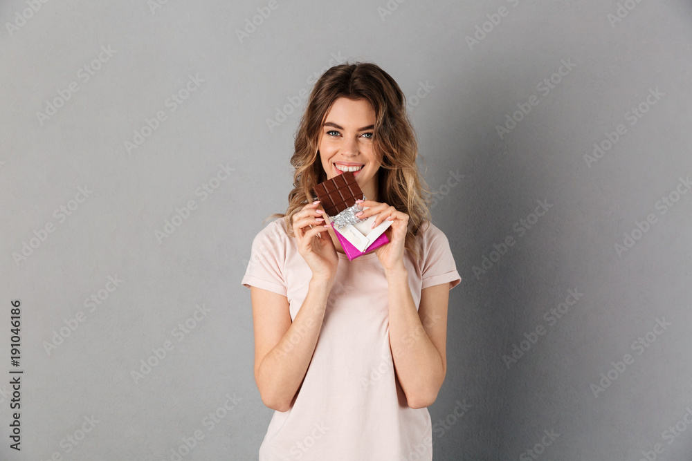 Smiling woman in t-shirt eating chocolate and looking at camera