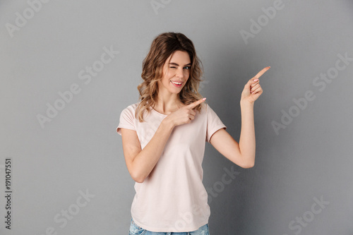 Smiling woman in t-shirt pointing away while winks