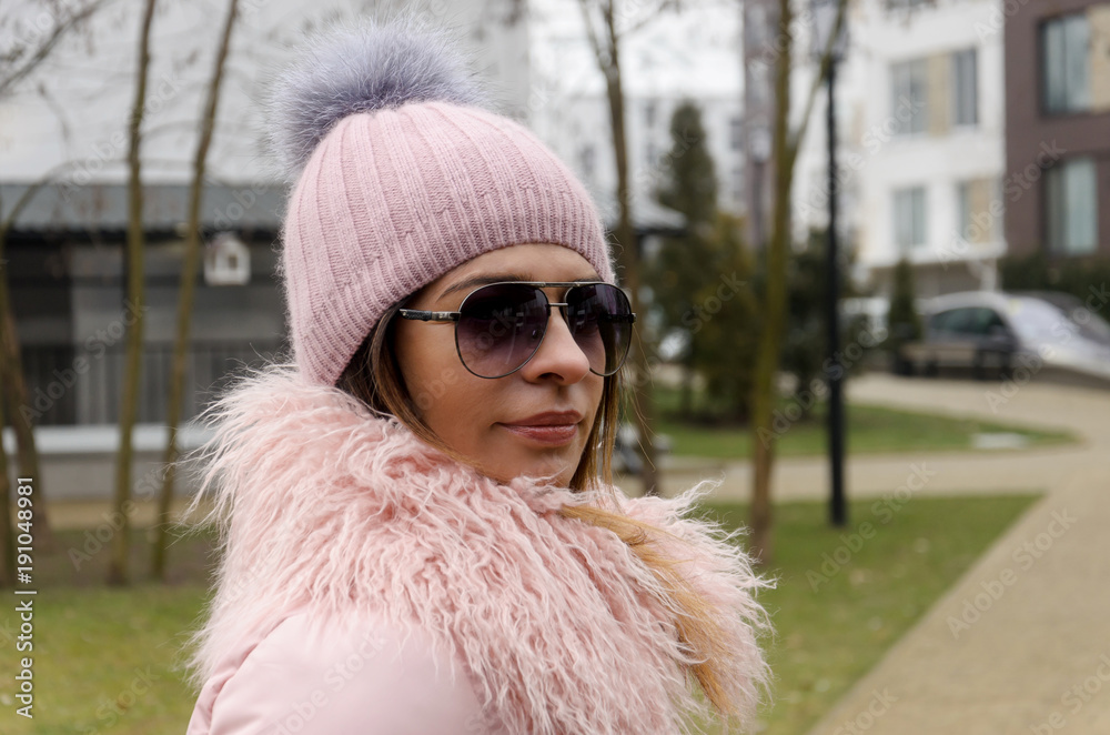 attractive woman in a pink winter jacket with a collar made of lama wool, sunglasses and a hat attractive woman in a pink winter jacket with a collar made of lama wool, sunglasses and a hat