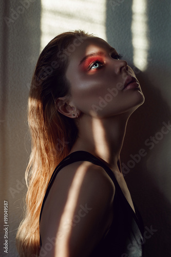 Art fashion contrast portrait of a woman near the window with a shadow on her face. Bright makeup, expressive emotions, mystical, mysterious way. Beautiful big eyes in the sun