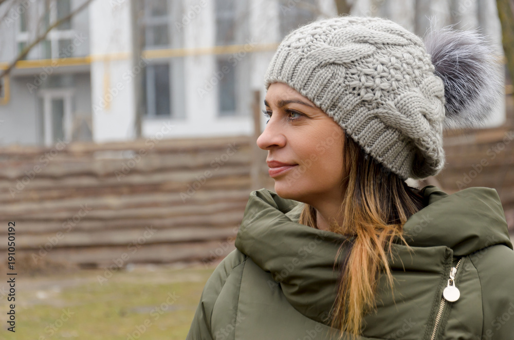 attractive woman in a green winter jacket and hat with a fashionable fur pompom walks