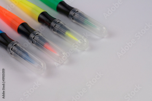 Row of colored marker brushes with transparent plastic tip on white school desk with copy space
