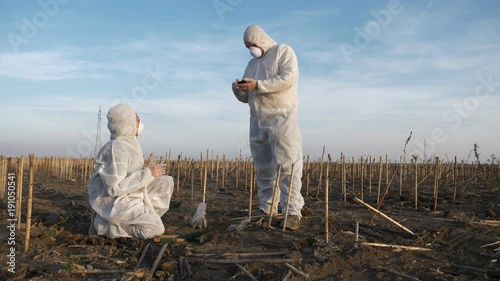 Slow motion footage of ecology specialists in white protection clothes observing and analyzing contaminated landscape, entering data on smartphone