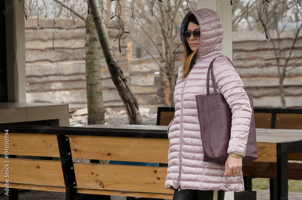 attractive woman is standing in a quilted winter pink jacket near a bessie in a country complex. Rest of the day off