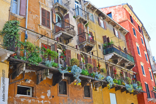 Beautiful traditional Italian building with flowers on balcony of medieval wall, Piazza delle Erbe, Verona, Italy