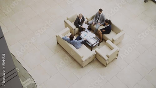 Top view of group of business people colleagues discussing financial charts sitting on couchs in lobby at modern business center photo