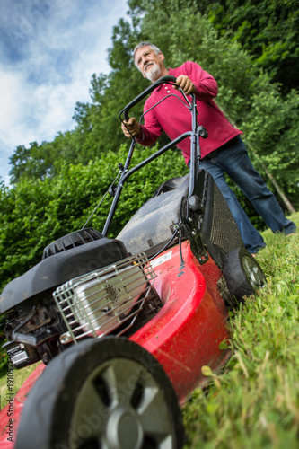 Senior man mowing the lawn in his garden