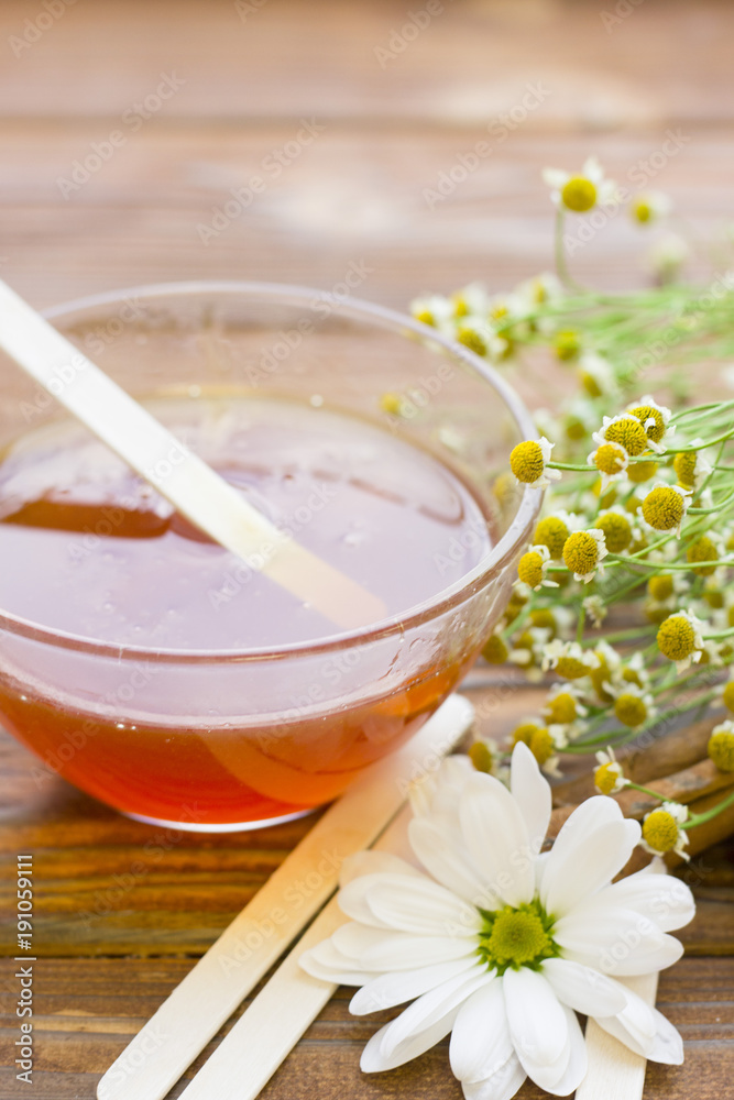 Set of sugaring essentials with natural honey, cinnamon sticks, and camomile on a natural dark wooden background Set of sugaring essentials with natural honey, cinnamon sticks, and camomile on a natural dark wooden background