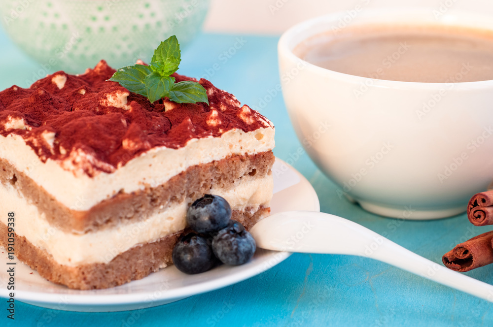 Italian tiramisu dessert on a porcelain plate, on a blue background Italian tiramisu dessert on a porcelain plate, on a blue background