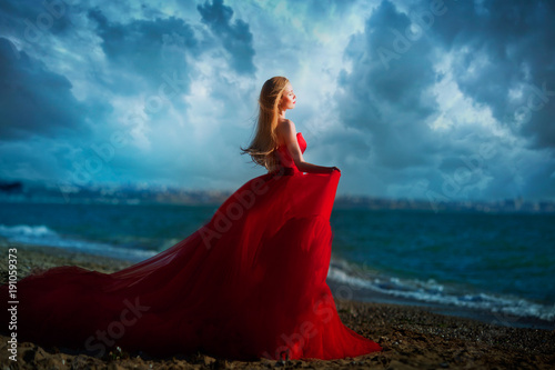 Beautiful girl by the sea. A woman in a red dress on the beach.