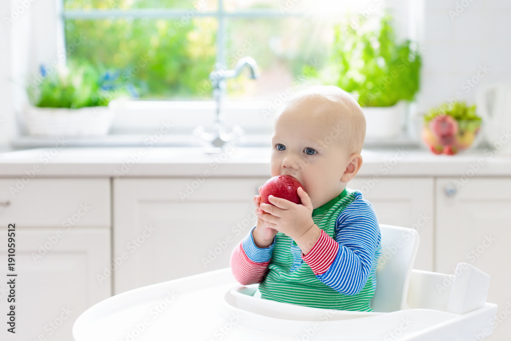 Baby boy eating apple in white kitchen at home Baby boy eating apple in white kitchen at home
