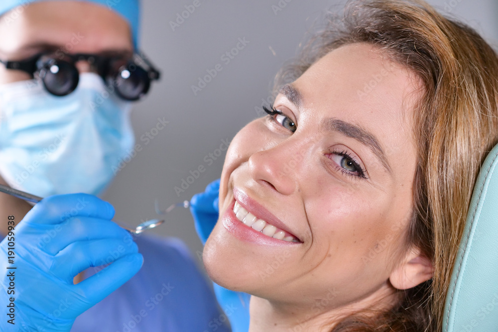 In a professional practice, a dentist checks the dentition of the patient, and she is happy with the visit, smiling, showing the perfect white teeth. Concept of: dentists, healthcare, perfect smile. In a professional practice, a dentist checks the dentition of the patient, and she is happy with the visit, smiling, showing the perfect white teeth. Concept of: dentists, healthcare, perfect smile.