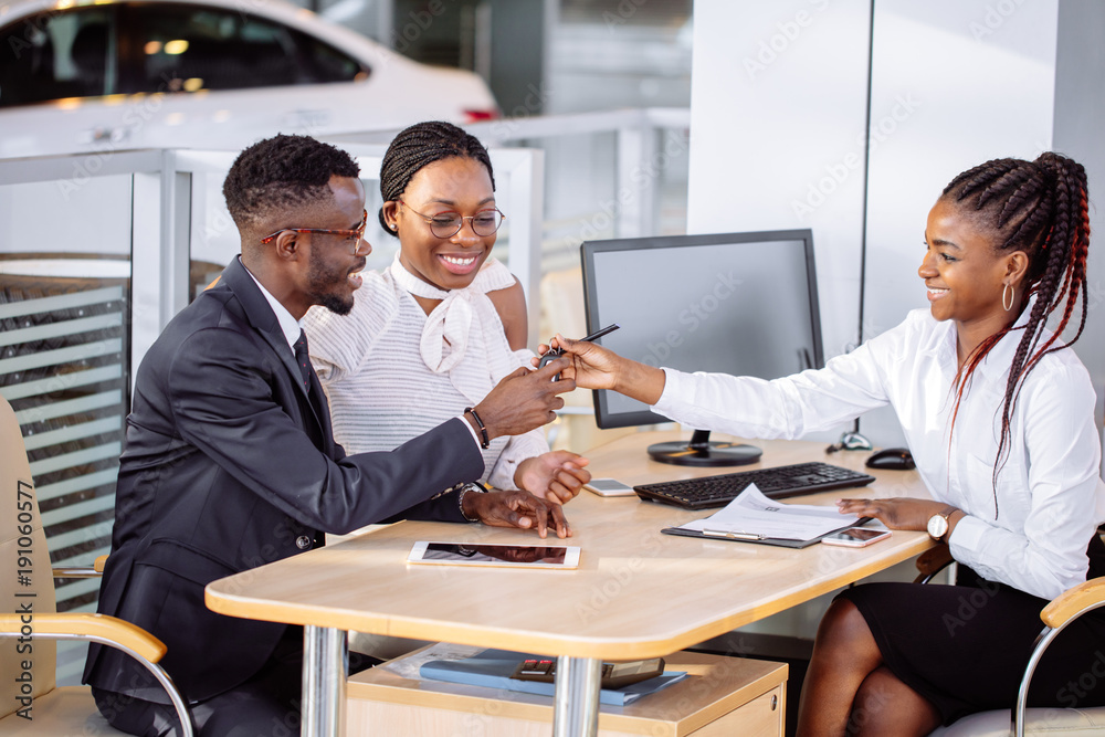 happy African couple and female seller sit at table and make a deal for sale of car happy African couple and female seller sit at table and make a deal for sale of car