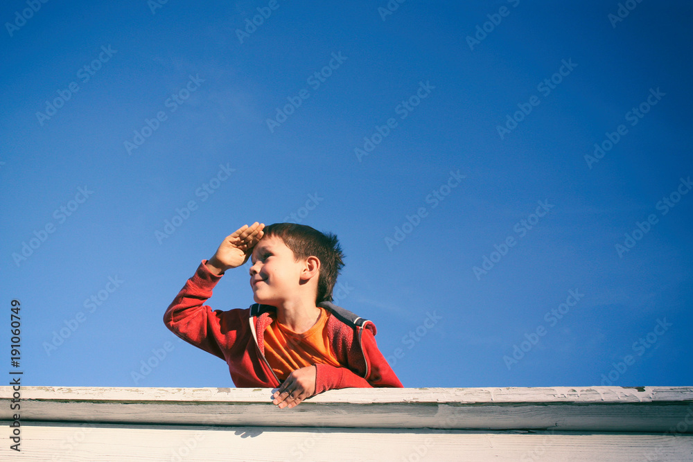 boy gazes into the distance. smiling boy on a background of bright blue sky on a sunny day. Copy space for your text boy gazes into the distance. smiling boy on a background of bright blue sky on a sunny day. Copy space for your text