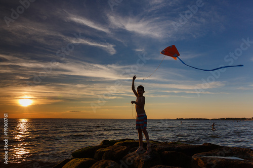 boy launches a kite on the seafront. Child silhouette with a kite on the beach at sunset. Copy space for your text