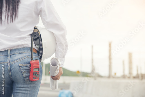 Construction engineer woman holding portable radio,blue print and safety helmet at construction site,wearing fashion jean inspect project at refinery plant.Construction Engineer woman concept.