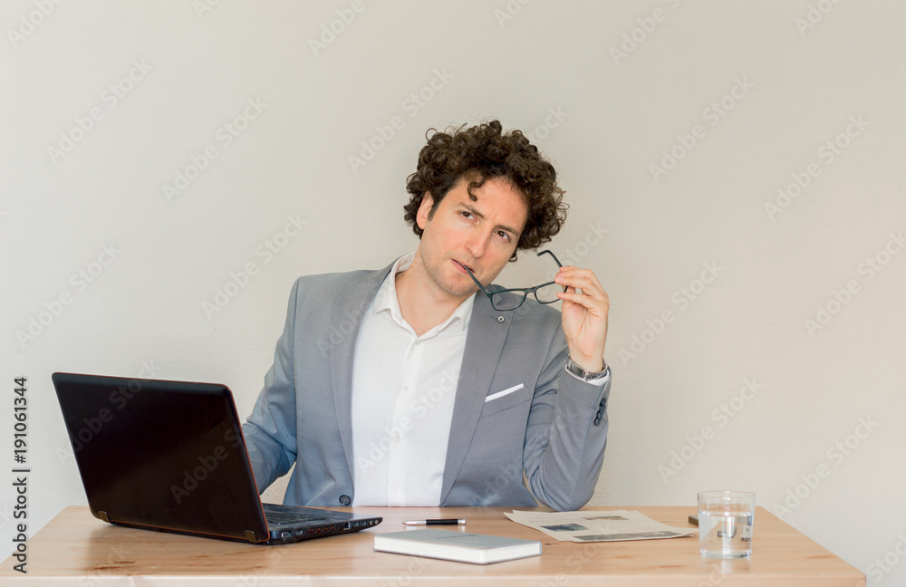 Young, Caucasian, serious businessman sitting at his desk in front of empty clear wall Young, Caucasian, serious businessman sitting at his desk in front of empty clear wall