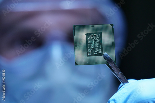 An Ultra Modern Electronic Manufacturing Factory Design Engineer in Sterile Coverall Holds Microchip with symbols in futuristic holography photo