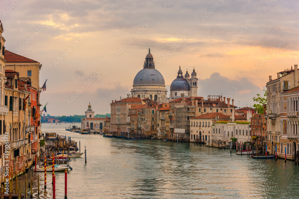Landscape sunset view of traditional Gondolas on famous Canal Grande with historic Basilica di Santa Maria della Salute in the background in romantic golden evening light at sunset in Venice,