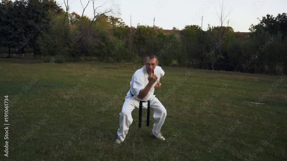 The man in Kimono Shows the Performance Technique of Kata Karate on Glade in the City Park Rano Morning The man in Kimono Shows the Performance Technique of Kata Karate on Glade in the City Park Rano Morning