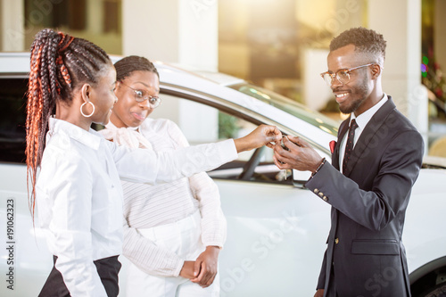 Young car african female salesman giving a key from the new car to the beautiful young african couple owners photo