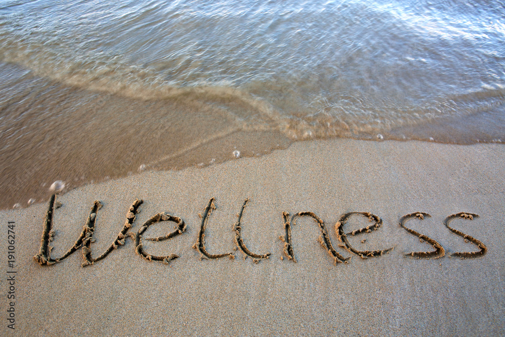 Fototapeta premium Word Wellness written on the sand near the sea.Vacation concept.