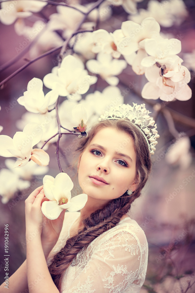 Beautiful young woman with crown in blossom magnolia garden. Spring.