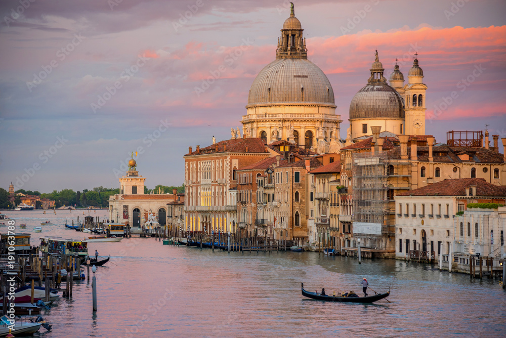 Beautiful landscape sunset view of traditional Gondolas on famous Canal Grande with historic Basilica di Santa Maria della Salute in the background in romantic evening at sunset in Venice, Italy